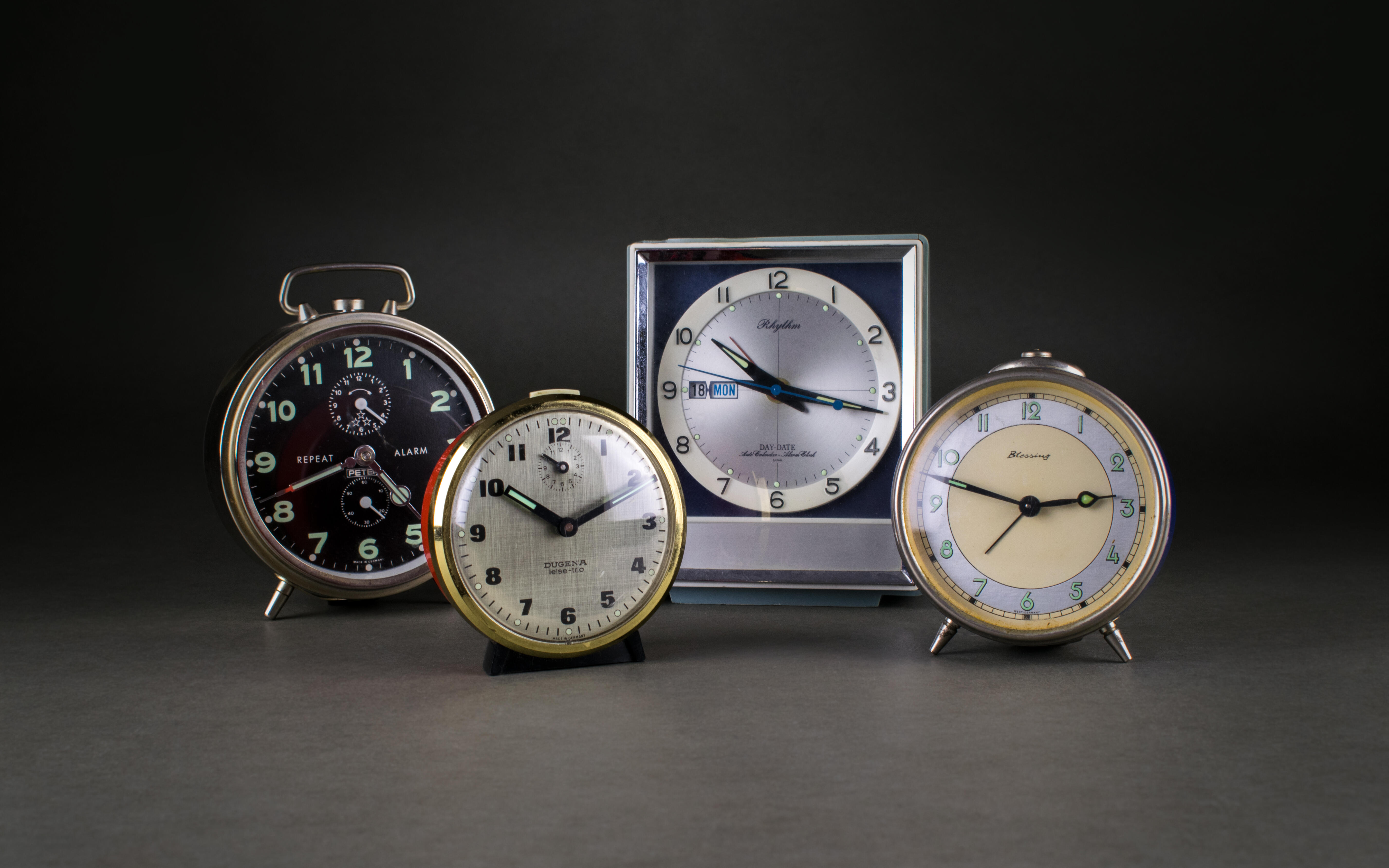 Auf dem Bild sind vier Wecker zu sehen, die sogenannte Gastarbeiter*innen in ihren Unterbringungen genutzt haben, um zu Arbeit zu kommen.