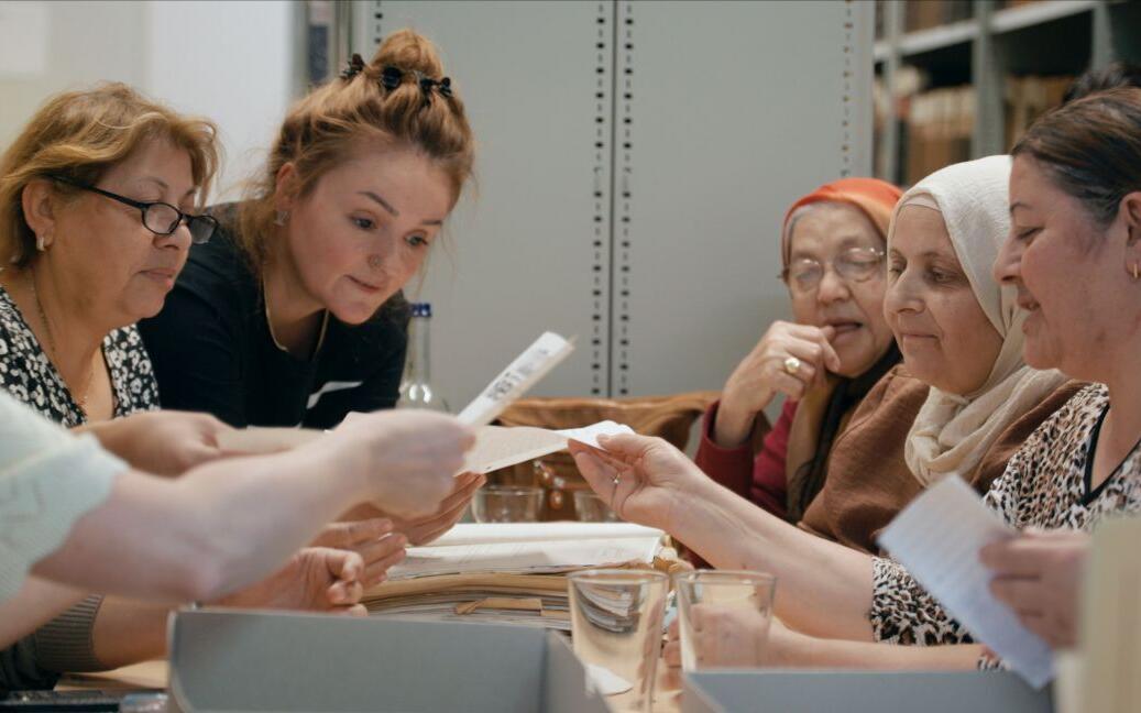 Six women sit opposite each other at a table and show copies of the ‘Möllner Briefe’ (Mölln Letters).
