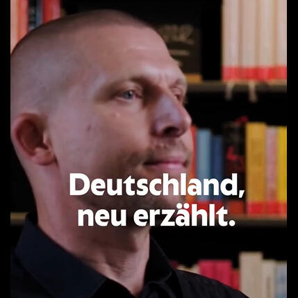Vor einer Bücherwand erzählt Georg Smirnov seine Geschichte. Auf dem Bild sieht man noch "Deutschland, neu erzählt", das Motto vom Museum Selma.
