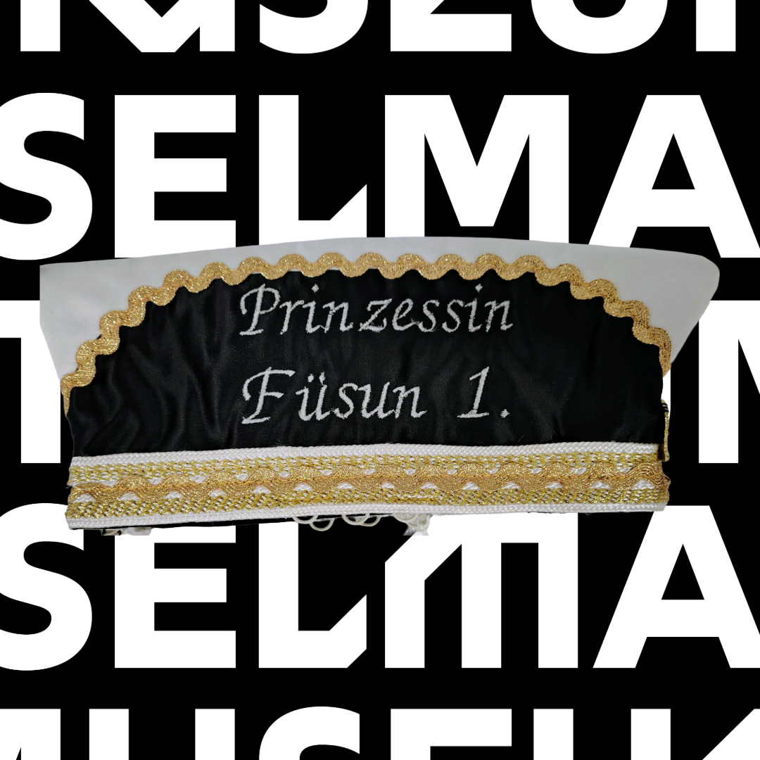 Eine Kopfbedeckung in schwarz, weiß und gold, die zu Karneval getragen wird. Darauf steht der Name der Karnevalsprinzessin Füsun, die Erste.