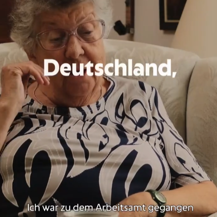 Eine Person sitzt auf einem Sofa, im Hintergrund hängen Bilder.